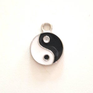 Könnte beinhalten: Ein silberner Anhänger mit einem schwarzen und weißen Yin-Yang-Symbol.