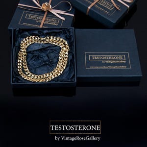 Puede incluir: Un collar de cadena dorado exhibido en una caja de regalo azul marino con tapa a juego, atado con una cinta marr&oacute;n claro y una flor dorada. La caja tiene el texto "TESTOSTERONE by VintageRoseGallery".