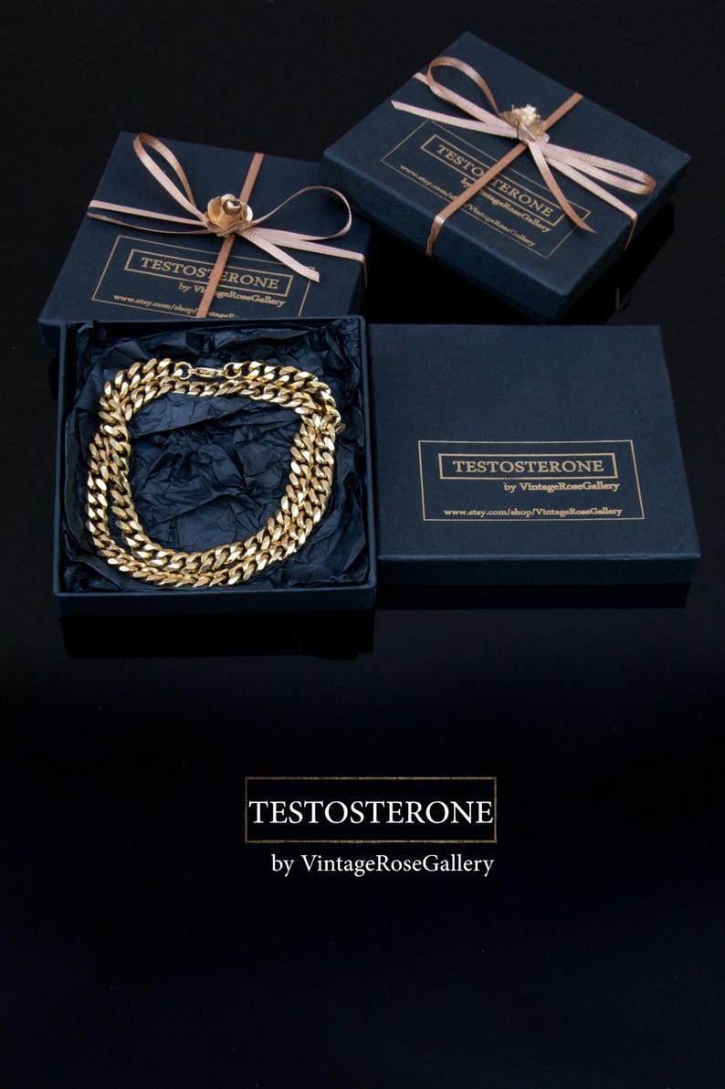 Puede incluir: Un collar de cadena dorado exhibido en una caja de regalo azul marino con tapa a juego, atado con una cinta marr&oacute;n claro y una flor dorada. La caja tiene el texto "TESTOSTERONE by VintageRoseGallery".