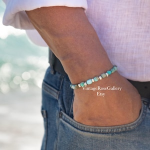 May include: A beaded bracelet featuring small, cylindrical turquoise-colored stones interspersed with tiny, polished silver-toned metal spacers. The bracelet is worn on a wrist, showcasing a repeating pattern of blue-green beads and metallic accents.