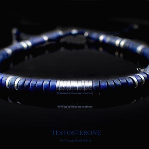 Puede incluir: Una pulsera de cuentas azul oscuro con detalles plateados. La pulsera presenta una serie de cuentas circulares azul oscuro intercaladas con anillos de metal plateado. La palabra "TESTOSTERONE" est&aacute; impresa en la parte inferior de la imagen.