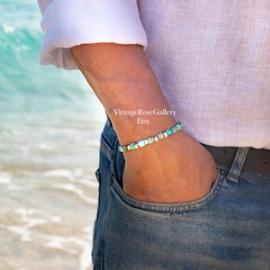 May include: A beaded bracelet featuring small, round turquoise-colored stones interspersed with metallic silver-toned spacers. The bracelet is worn on a wrist, with the text VintageRoseGallery Etsy visible in the center of the image.