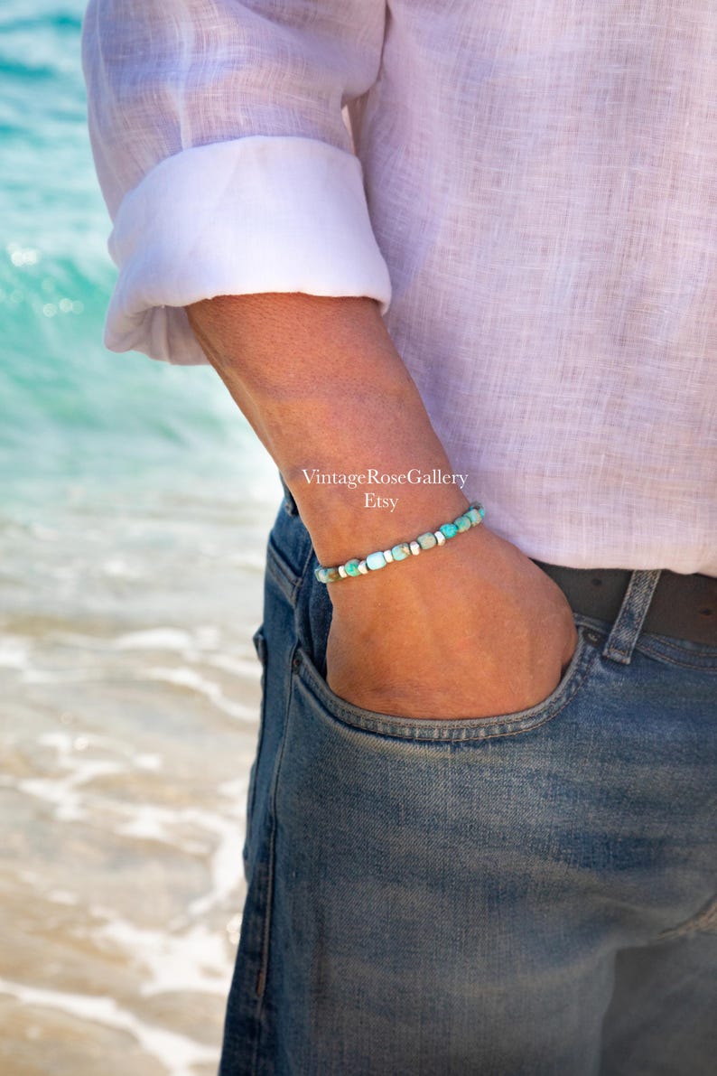 May include: A beaded bracelet featuring small, round turquoise-colored stones interspersed with metallic silver-toned spacers. The bracelet is worn on a wrist, with the text VintageRoseGallery Etsy visible in the center of the image.