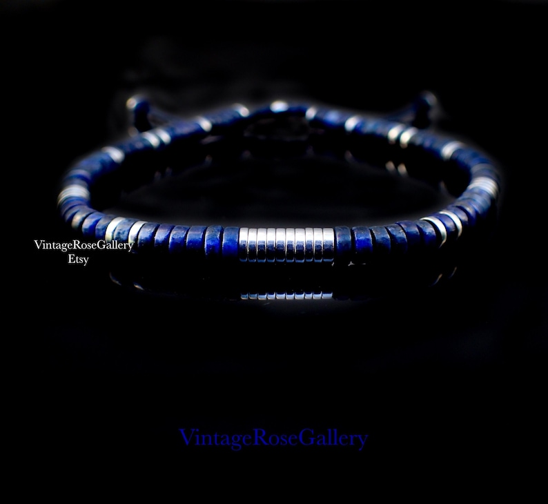 Puede incluir: Una pulsera azul oscuro con detalles plateados. La pulsera presenta peque&ntilde;as cuentas cuadradas azules y cuentas cil&iacute;ndricas plateadas. La pulsera se muestra sobre un fondo negro. El texto "VintageRoseGallery Etsy" es visible.