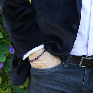 May include: A bracelet with purple and silver beads is worn on a wrist. The person is wearing a black blazer, a white collared shirt, and dark blue jeans. The Etsy shop name "VintageRoseGallery" is visible.
