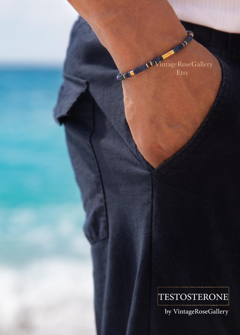 Puede incluir: Una pulsera de cuentas azul marino con detalles dorados. La pulsera se lleva en la mu&ntilde;eca, con un bolsillo azul marino en el fondo. El oc&eacute;ano es visible. El texto "TESTOSTERONE" est&aacute; en la parte inferior.