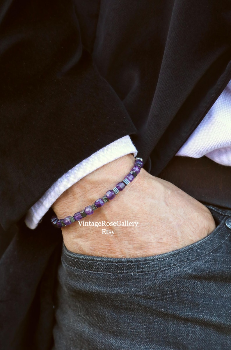 May include: A bracelet with purple gemstones and silver-coloured metal beads. The bracelet is worn on a wrist, visible against a white shirt cuff and a black jacket. The Etsy shop name is visible.