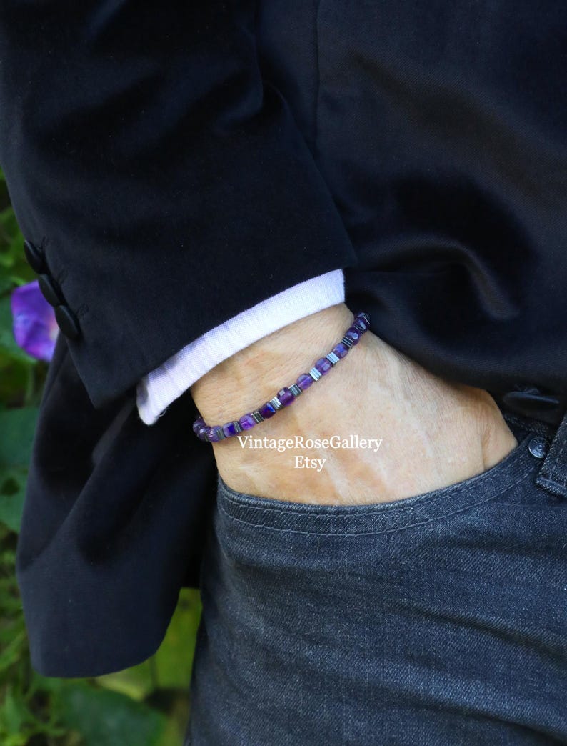 May include: A bracelet featuring purple and silver beads. The bracelet is worn on a wrist, with a black blazer and white shirt cuff visible. The person is wearing dark wash jeans. The Etsy shop name "VintageRoseGallery" is visible.