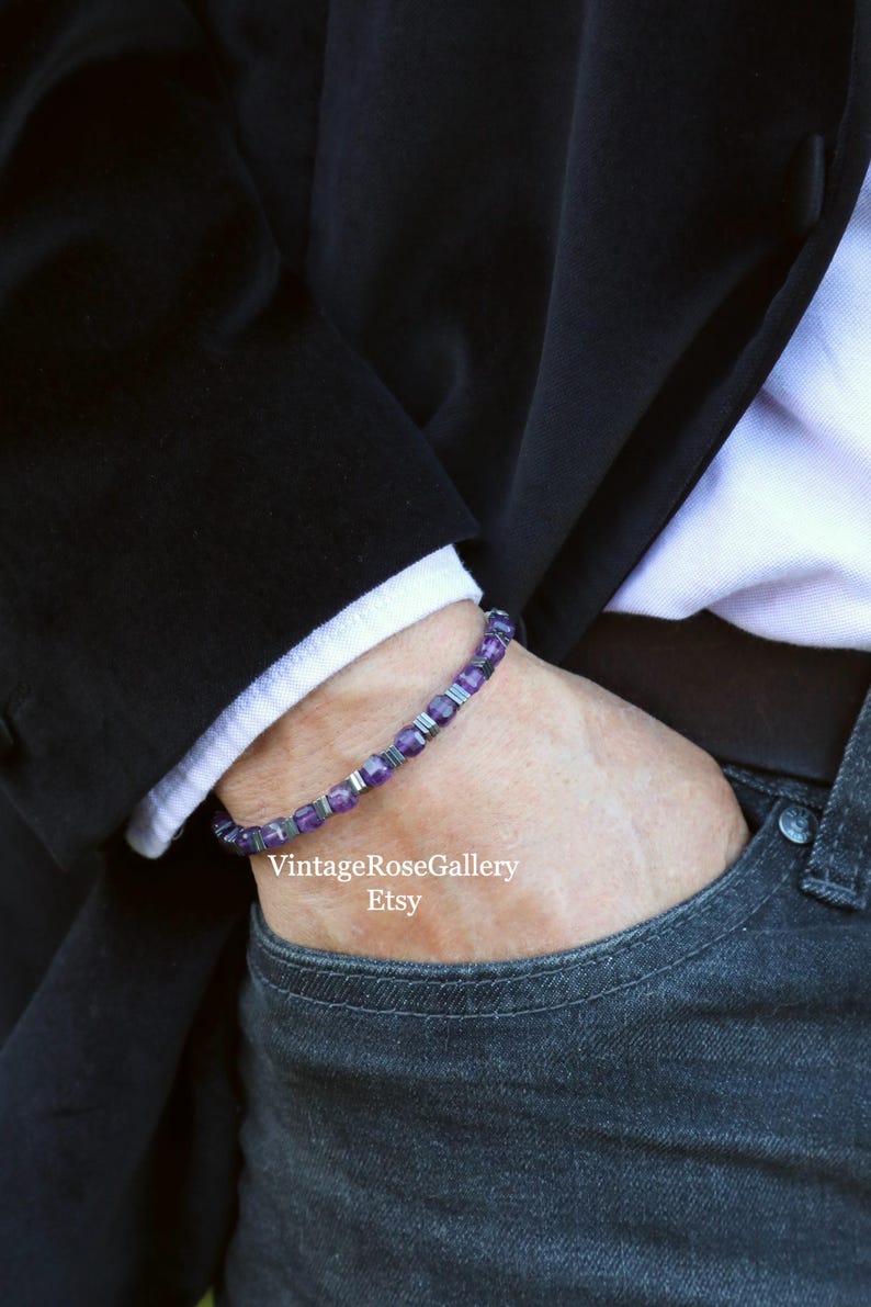 May include: A bracelet featuring purple and silver beads. The bracelet is worn on a wrist, with a black blazer and white shirt cuff visible. The Etsy shop name is visible in the image.