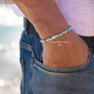 May include: A beaded bracelet featuring alternating turquoise-colored stone beads and small metallic silver-toned spacers. The bracelet is worn on a wrist and includes the text VintageRoseGallery Etsy printed in white on the image surface.