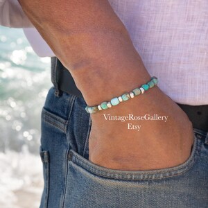 May include: A beaded bracelet featuring small, rectangular turquoise-colored stones interspersed with smooth, metallic silver-toned cylindrical spacers. The bracelet is worn on a wrist, and the text VintageRoseGallery Etsy is visible.