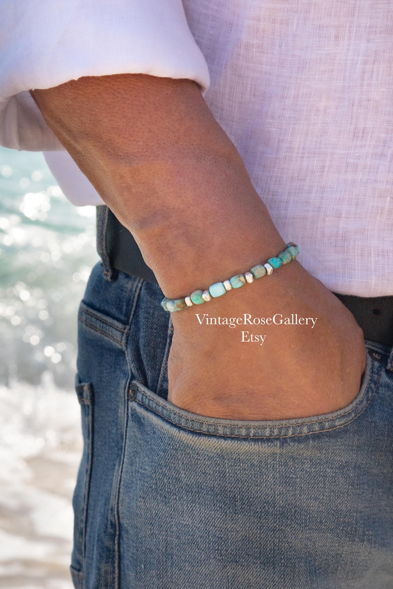 May include: A beaded bracelet featuring small, rectangular turquoise-colored stones interspersed with smooth, metallic silver-toned cylindrical spacers. The bracelet is worn on a wrist, and the text VintageRoseGallery Etsy is visible.