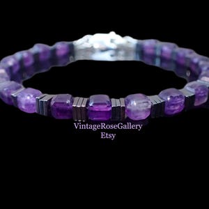 May include: A purple beaded bracelet with a silver clasp. The bracelet features square-cut amethyst stones and silver-coloured metal spacers. The text "VintageRoseGallery Etsy" is visible in the image.