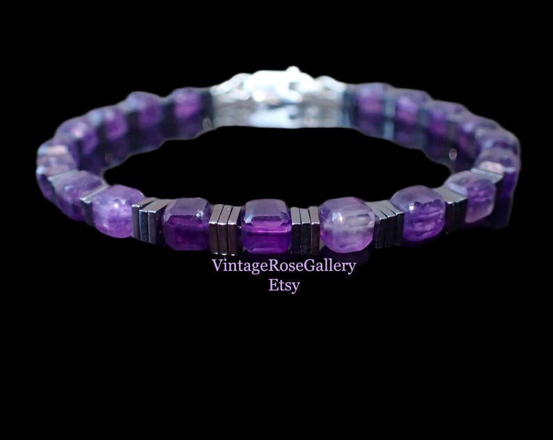 May include: A purple beaded bracelet with a silver clasp. The bracelet features square-cut amethyst stones and silver-coloured metal spacers. The text "VintageRoseGallery Etsy" is visible in the image.