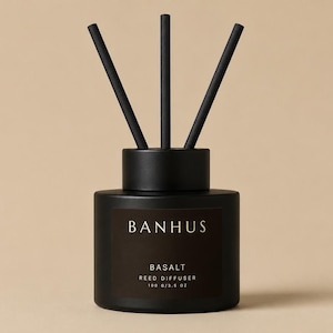 Peut inclure: Un flacon diffuseur à roseaux noir mat avec trois bâtonnets noirs insérés. L'étiquette porte le texte BANHUS, BASALT, REED DIFFUSER et 100 g/3,5 oz en lettres blanches. Le récipient cylindrique possède un bouchon noir assorti.