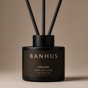 Peut inclure: Un diffuseur à roseaux noir mat avec trois bâtonnets noirs. L'étiquette porte le texte BANHUS, GRUNN, REED DIFFUSER et 100 g/3.5 oz en lettres blanches. La bouteille a une forme cylindrique avec un bouchon noir assorti sur le dessus.
