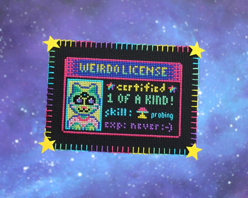 Op de afbeelding: Een kruissteek "Weirdo License" met een cartoon alien karakter. De zwarte achtergrond is omlijst met kleurrijke steken en gele steraccenten. De licentietekst bevat "gecertificeerd", "1 of a kind" en "probing" als vaardigheid.