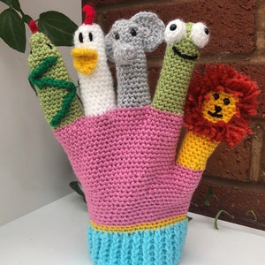 Peut inclure: Un gant de marionnette à doigts en crochet rose avec cinq marionnettes à doigts : un serpent vert, une poule blanche, un éléphant gris, une grenouille verte et un lion jaune avec une crinière rouge.
