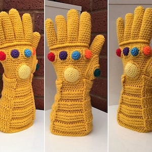 May include: A crocheted yellow glove with a gold colour, resembling the Infinity Gauntlet from the Marvel Cinematic Universe. The glove has six colourful gemstones on the knuckles.