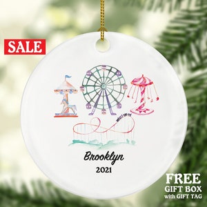 May include: White ceramic Christmas ornament with a watercolor illustration of a Ferris wheel, carousel, and roller coaster. The ornament is personalized with the name "Brooklyn" and the year "2021".