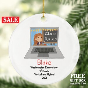 May include: White ceramic Christmas ornament with a cartoon illustration of a girl teaching online. The ornament says "Class Rules" on a chalkboard and "Blake Westminster Elementary 4th Grade Virtual and Hybrid 2021".