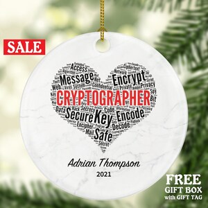 May include: White round ceramic Christmas ornament with a black and white heart-shaped word cloud that says "CRYPTOGRAPHER" in red. The word cloud includes words like "encrypt", "secure", "key", "code", "safe", and "privacy". The ornament also has the text "Adrian Thompson 2021" printed on it.
