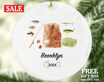May include: White ceramic Christmas ornament with a watercolor illustration of fishing gear, including a fishing vest, fishing rod, lures, and a tackle box. The ornament is personalized with the name "Brooklyn" and the year "2021".