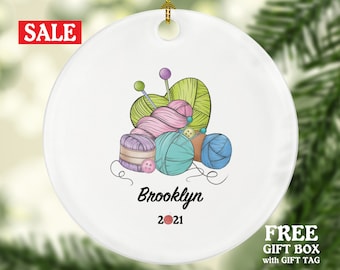 May include: White ceramic ornament with a colorful illustration of yarn, needles, and buttons. The ornament is personalized with the name "Brooklyn" and the year "2021".