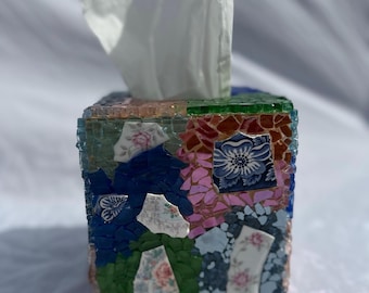 May include: A square tissue box cover made of mosaic glass tiles. The tiles are in shades of blue, green, pink, and brown. The box has a floral pattern.