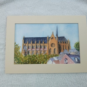 Könnte beinhalten: Aquarellmalerei einer großen, gelben Kirche mit einem hohen Turm und vielen Fenstern. Die Kirche ist von grünen Bäumen und kleineren Gebäuden umgeben.