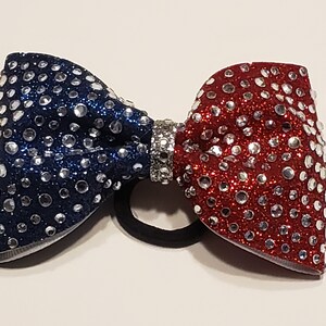 May include: A red and blue sparkly hair bow with a silver rhinestone center. The bow is attached to a black elastic hair tie.