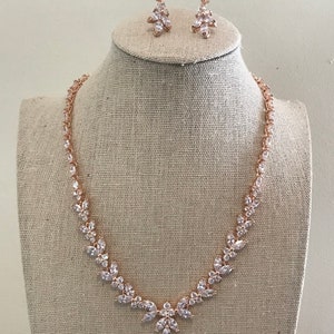 May include: A rose gold necklace and earrings set with clear cubic zirconia stones. The necklace features a teardrop pendant and a delicate chain.