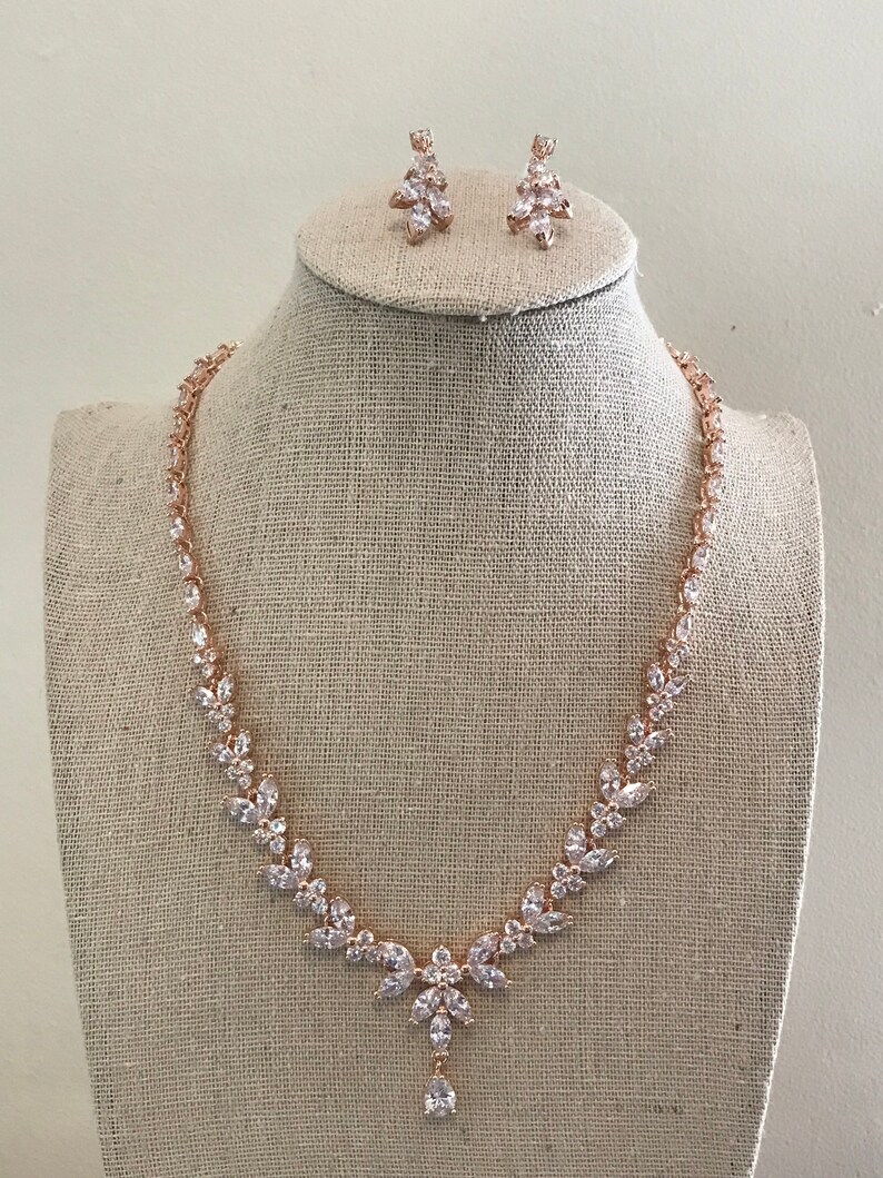 May include: A rose gold necklace and earrings set with clear cubic zirconia stones. The necklace features a teardrop pendant and a delicate chain.