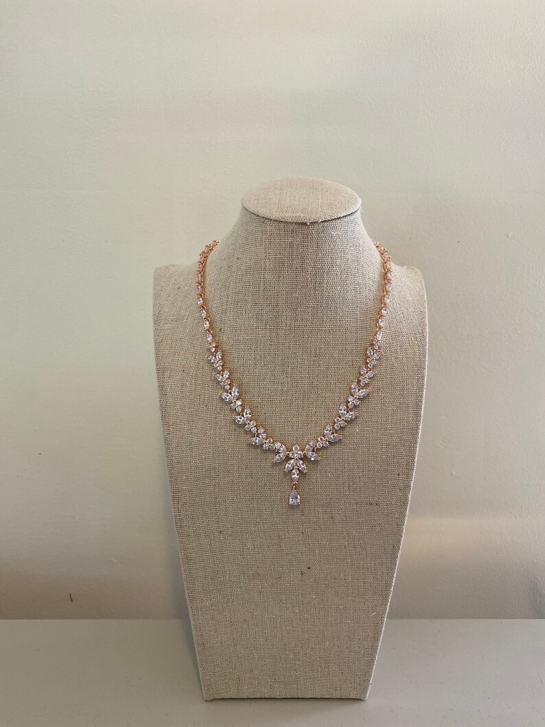 May include: A rose gold necklace with a teardrop pendant and clear cubic zirconia stones.