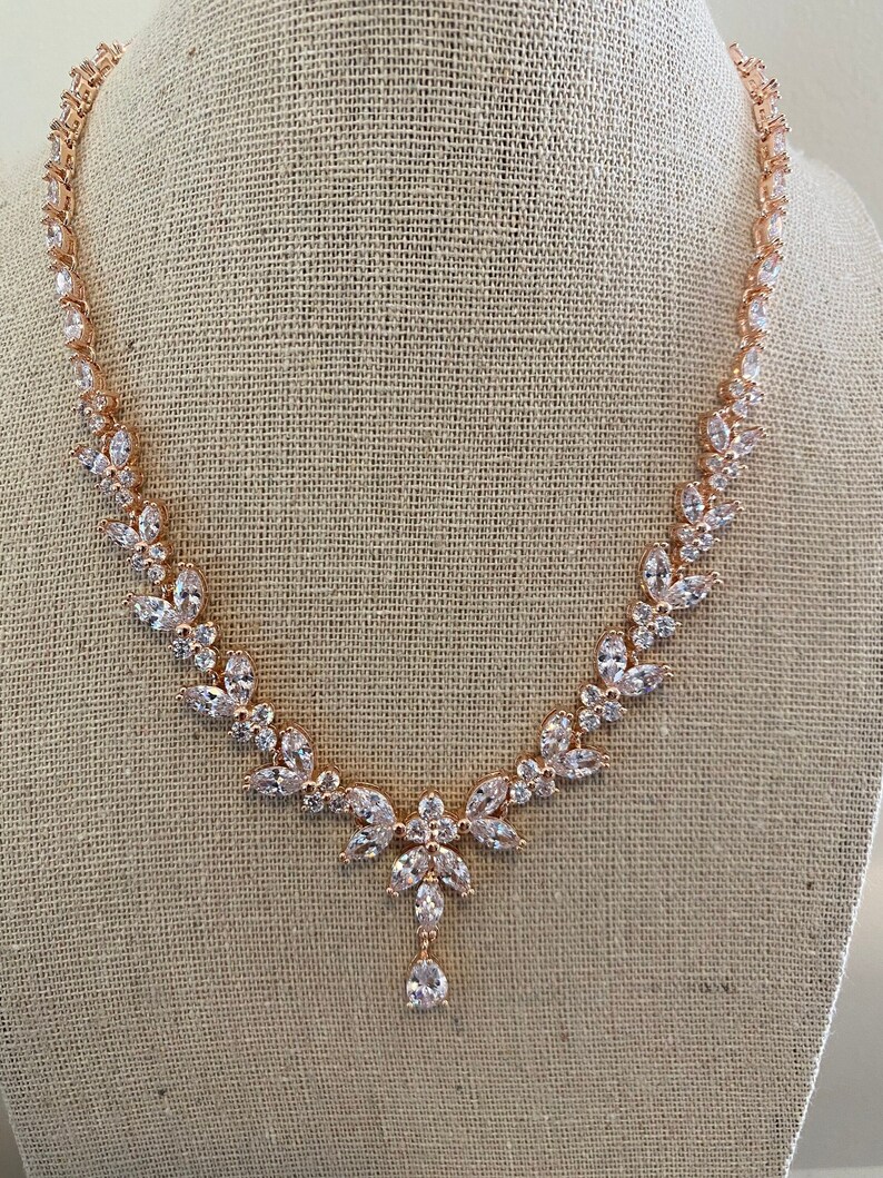 May include: A rose gold necklace with a teardrop pendant and a floral design. The necklace is made of cubic zirconia stones.
