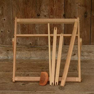 May include: A wooden weaving loom with various tools, including shuttles, a comb, and a ruler. The loom is light brown and set against a wooden background. The tools are arranged beside the loom, ready for use. The image showcases the craft of weaving.
