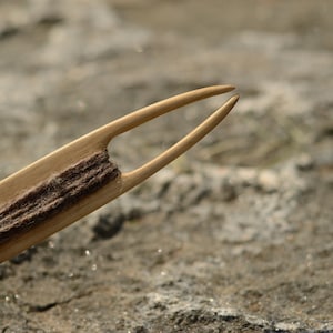 Könnte beinhalten: Ein Werkzeug aus Holz mit einem gegabelten Ende und einer Rille zum Halten von Garn. Das Werkzeug wird zum Weben oder Stricken verwendet.