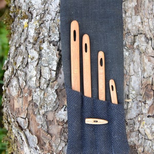 May include: Four wooden needle threaders of varying sizes are arranged in a black fabric pouch. The pouch has a small wooden button closure.