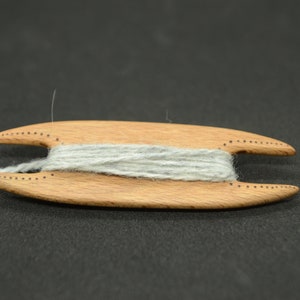 May include: A wooden yarn winder with a gray yarn wound around it.