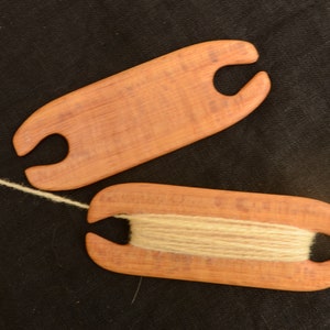 May include: Two wooden yarn winders. One winder is empty and the other has a length of white yarn wound around it.