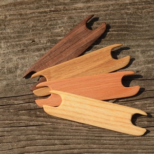 Peut inclure: Quatre aiguilles à tricoter en bois de différentes nuances de brun, disposées en éventail sur une surface en bois rustique.