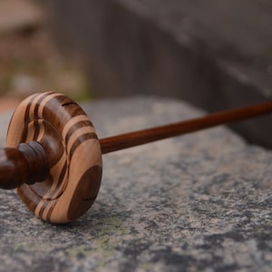 May include: A wooden spinning wheel with a brown and light brown striped spindle and a brown wooden handle.