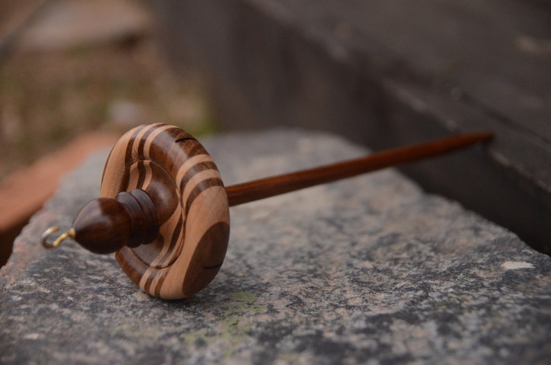 May include: A wooden spinning wheel with a brown and light brown striped spindle and a brown wooden handle.