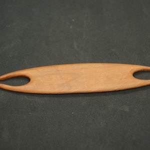 Peut inclure: Un outil de tissage en bois avec deux pointes à une extrémité. L'outil est brun et a une finition lisse et polie.