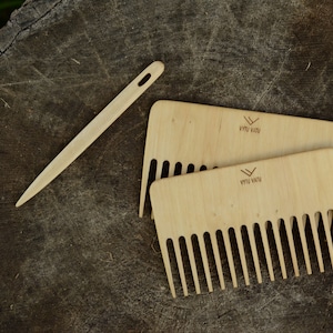 May include: A wooden hair pin and two wooden combs with closely spaced teeth, resting on a weathered, dark brown wood surface. The combs have the text "VYTU VATU" printed on them. The pin is long and slender.