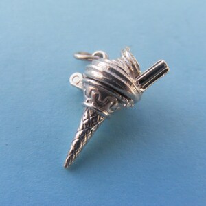 May include: A silver-toned ice cream cone charm with a detailed waffle cone and soft-serve ice cream design. The charm includes a loop for attaching to a bracelet or necklace. The background is a solid light blue.