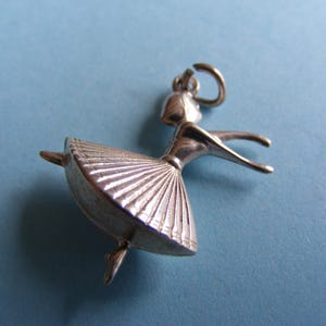 Peut inclure: Charm de ballerine argenté. Le charme représente une danseuse dans une pose gracieuse, les bras tendus et une jupe plissée. Le charme est suspendu à une petite boucle, prêt à être ajouté à un collier ou un bracelet.