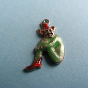 May include: A vintage charm in the shape of a seated elf. The elf is depicted with a smiling face, wearing a red hat and boots, and a green outfit. The charm is made of metal and has a loop for attaching to a bracelet or necklace.