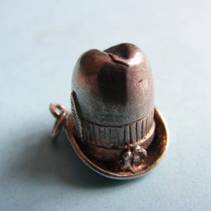 Peut inclure: Un petit charme argenté en forme de chapeau melon. Le chapeau présente une calotte arrondie, un bord et des détails décoratifs. Une petite boucle est attachée pour une utilisation en pendentif ou en breloque.