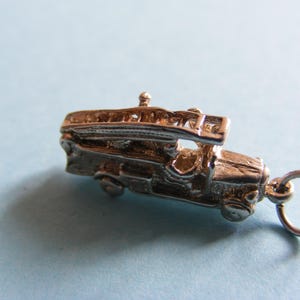 May include: A silver-coloured charm in the shape of a vintage fire engine. The charm has detailed features including a ladder, wheels, and a loop for attaching to a bracelet or necklace. The charm is set against a light blue background.